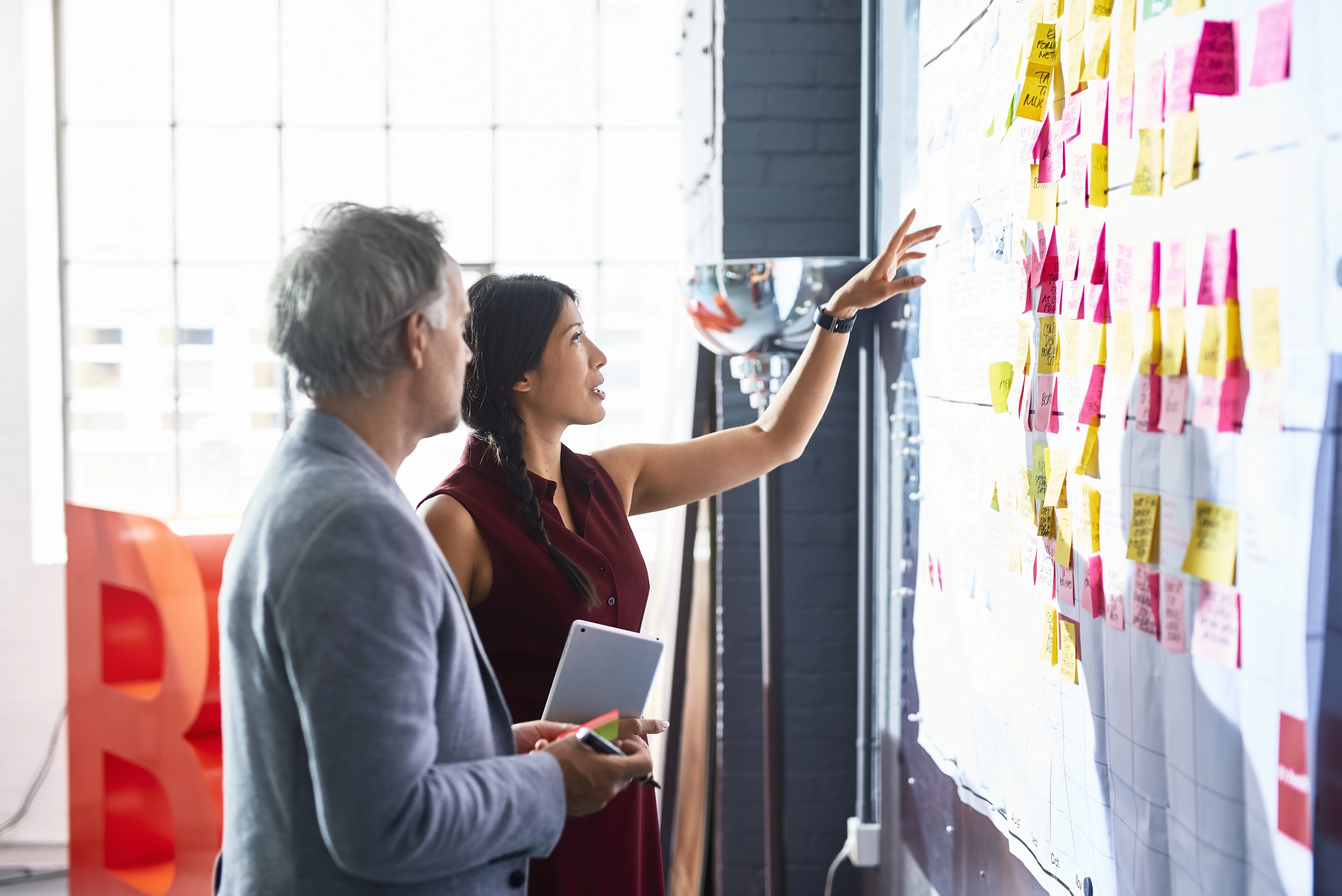 Man and woman looking at colorful adhensive notes on whiteboard in creative studio