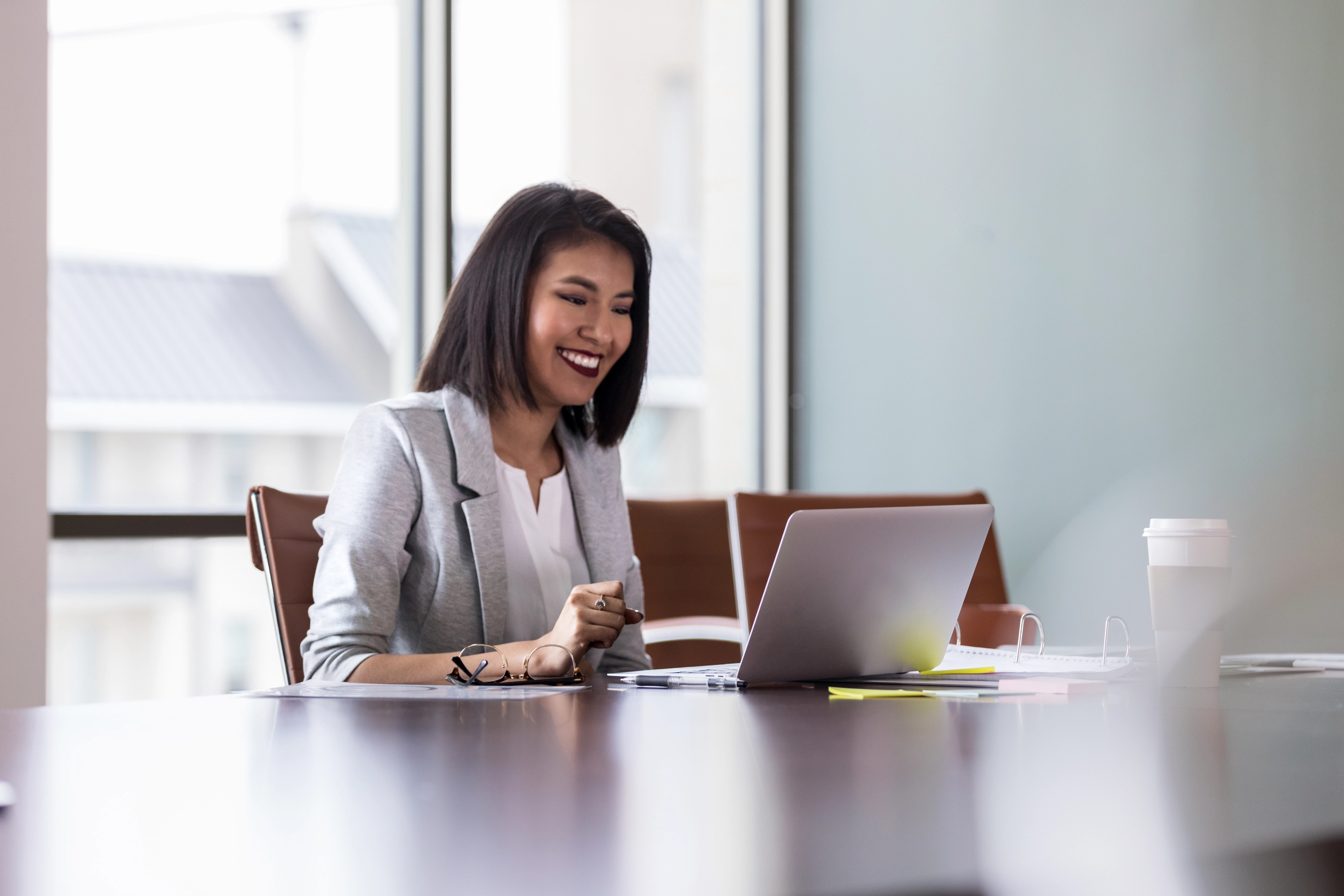 Beautiful young businesswoman smiles as she participates in a video conference with a colleague. She is using a laptop.