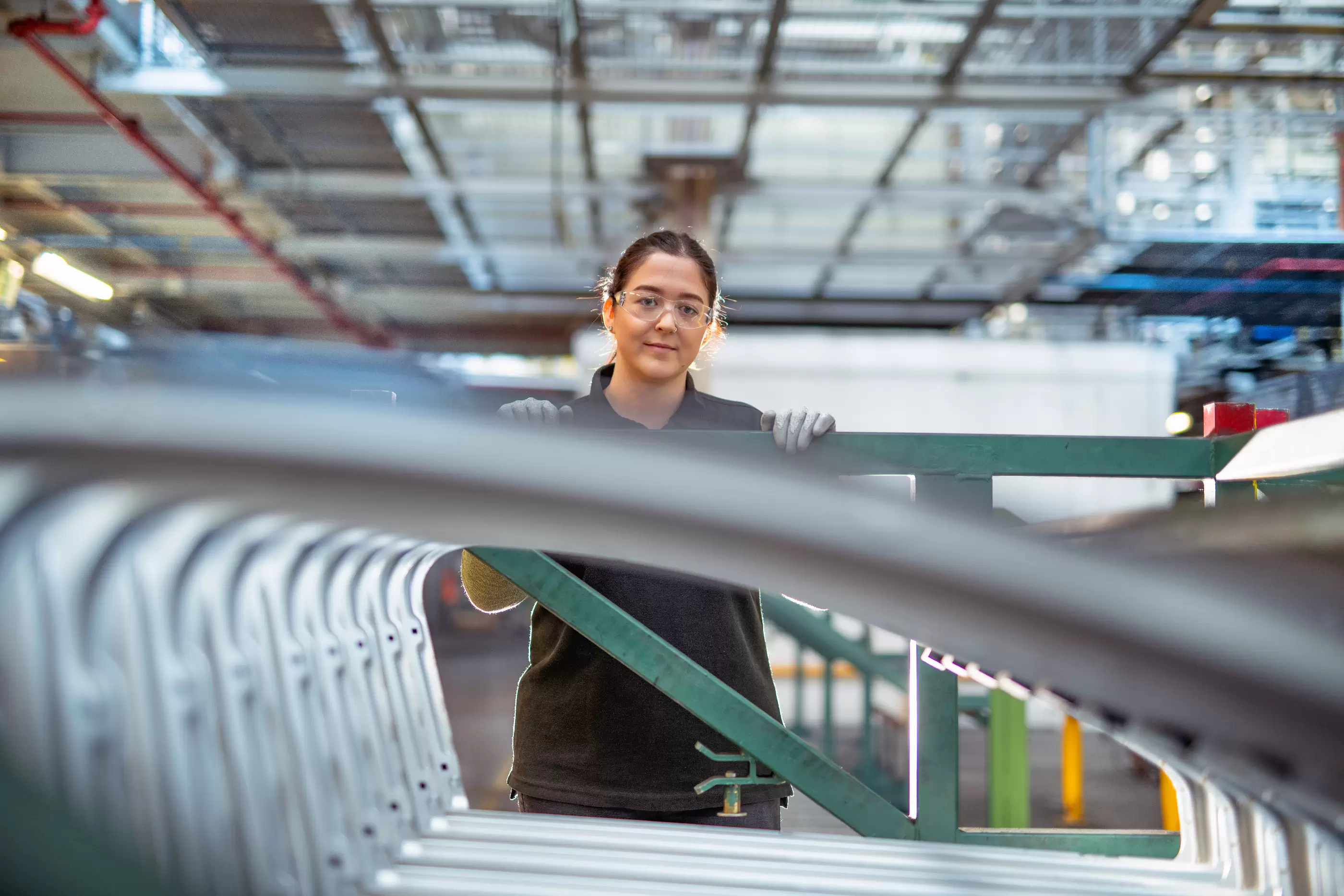 Portrait of female apprentice with car parts in car factory.