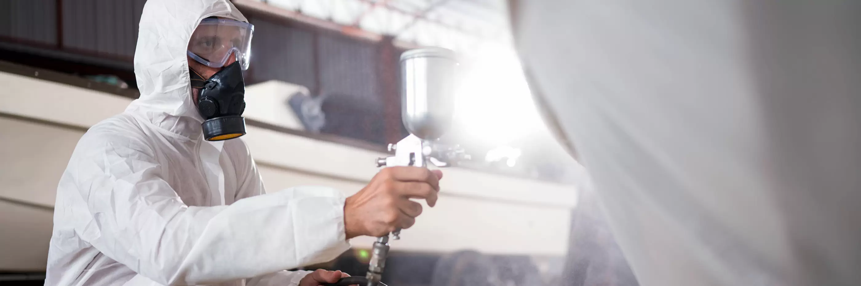 Man applying color on a boat hull outer surface by paint spray gun.