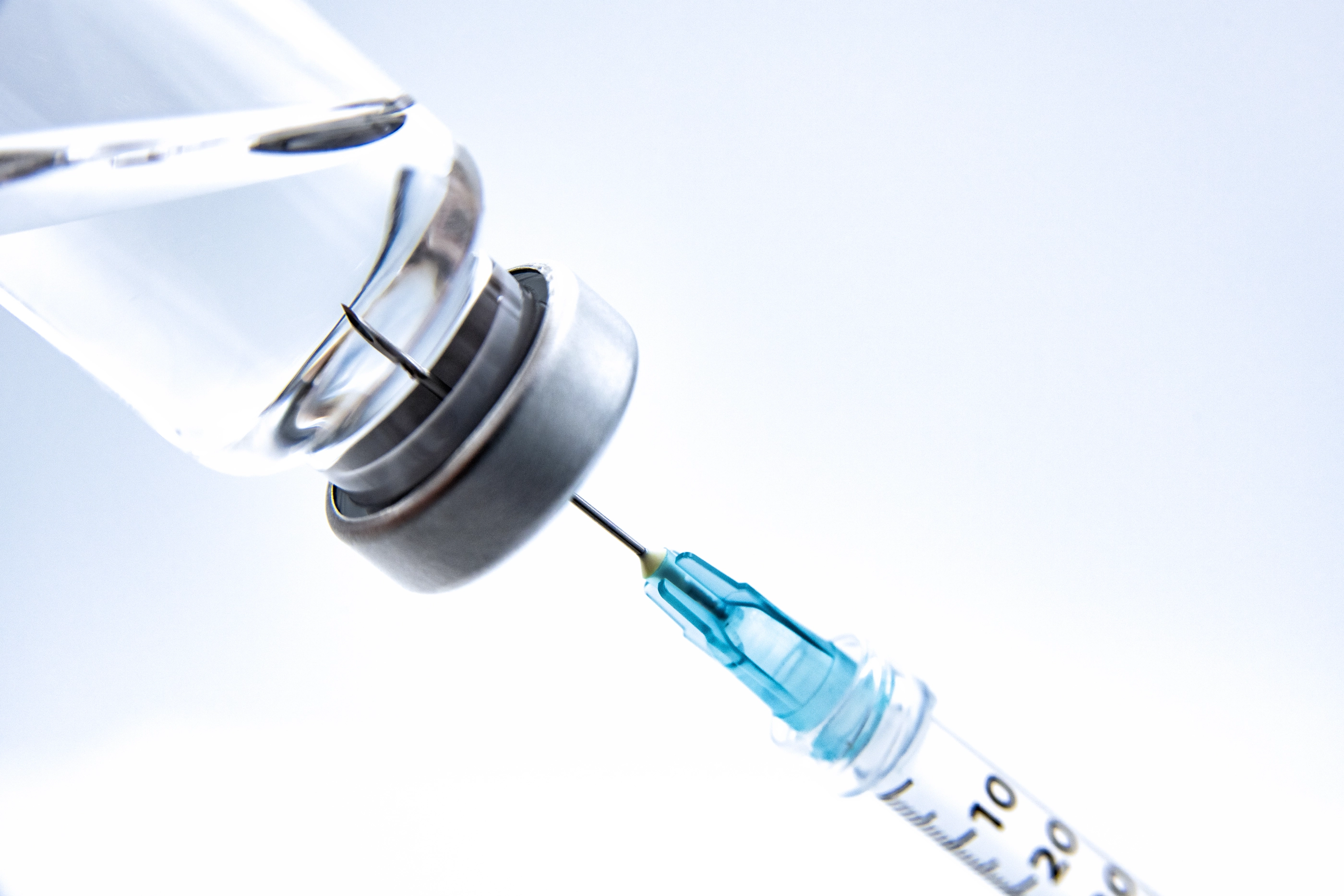 A medical vial of vaccine with a syringe arranged in studio against a white background.