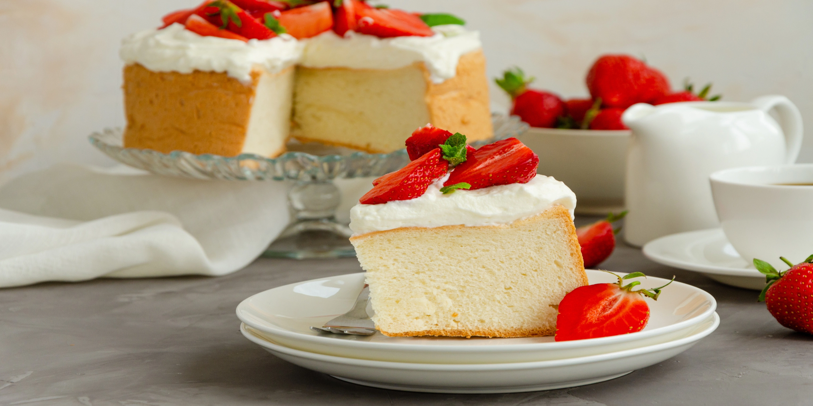 Angel food cake with whipped cream and slices of fresh strawberries on top on a concrete background. Summer dessert. Horizontal orientation, copy space