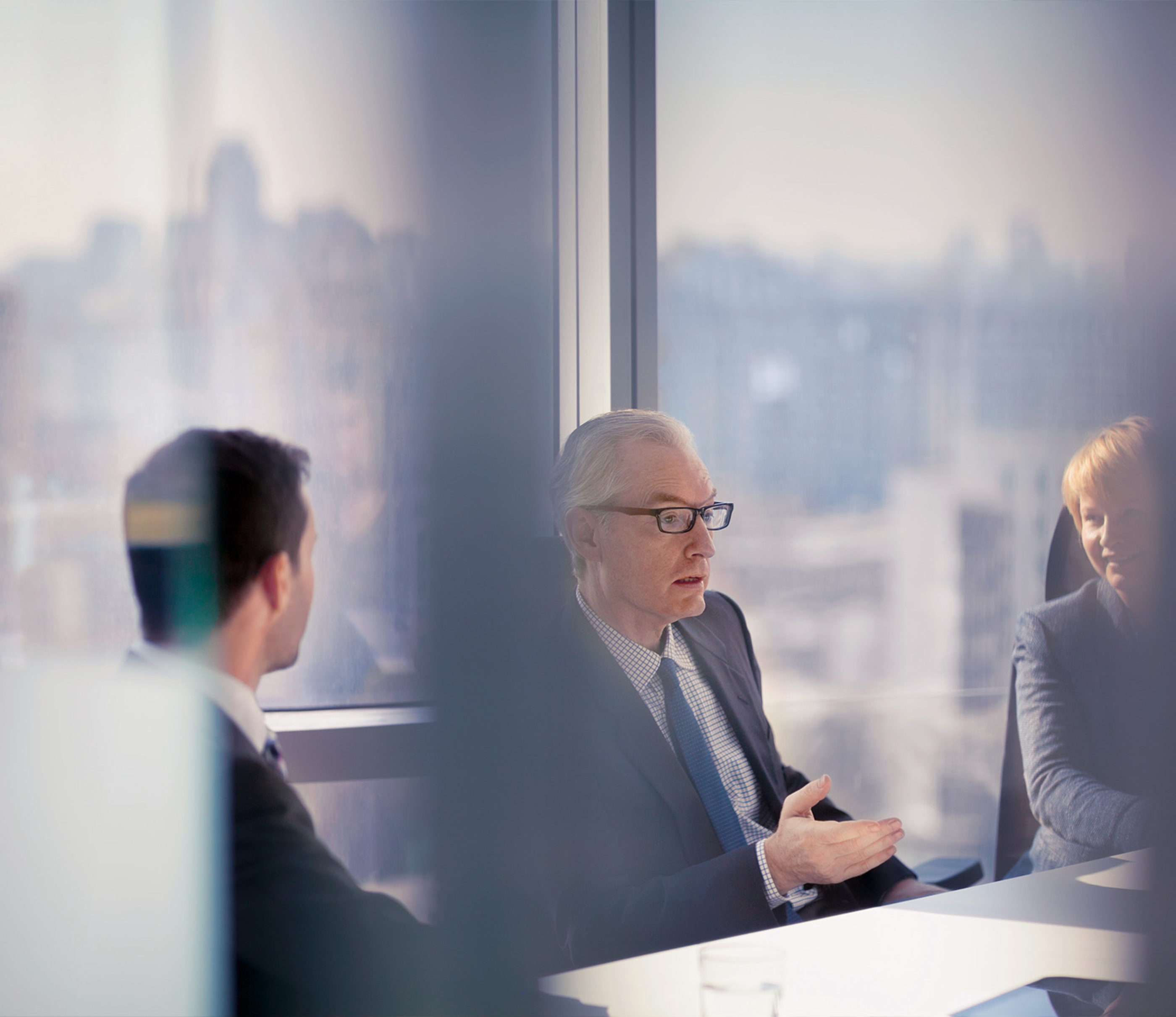 Through the glass view of businessman talking to colleagues in conference room meeting.