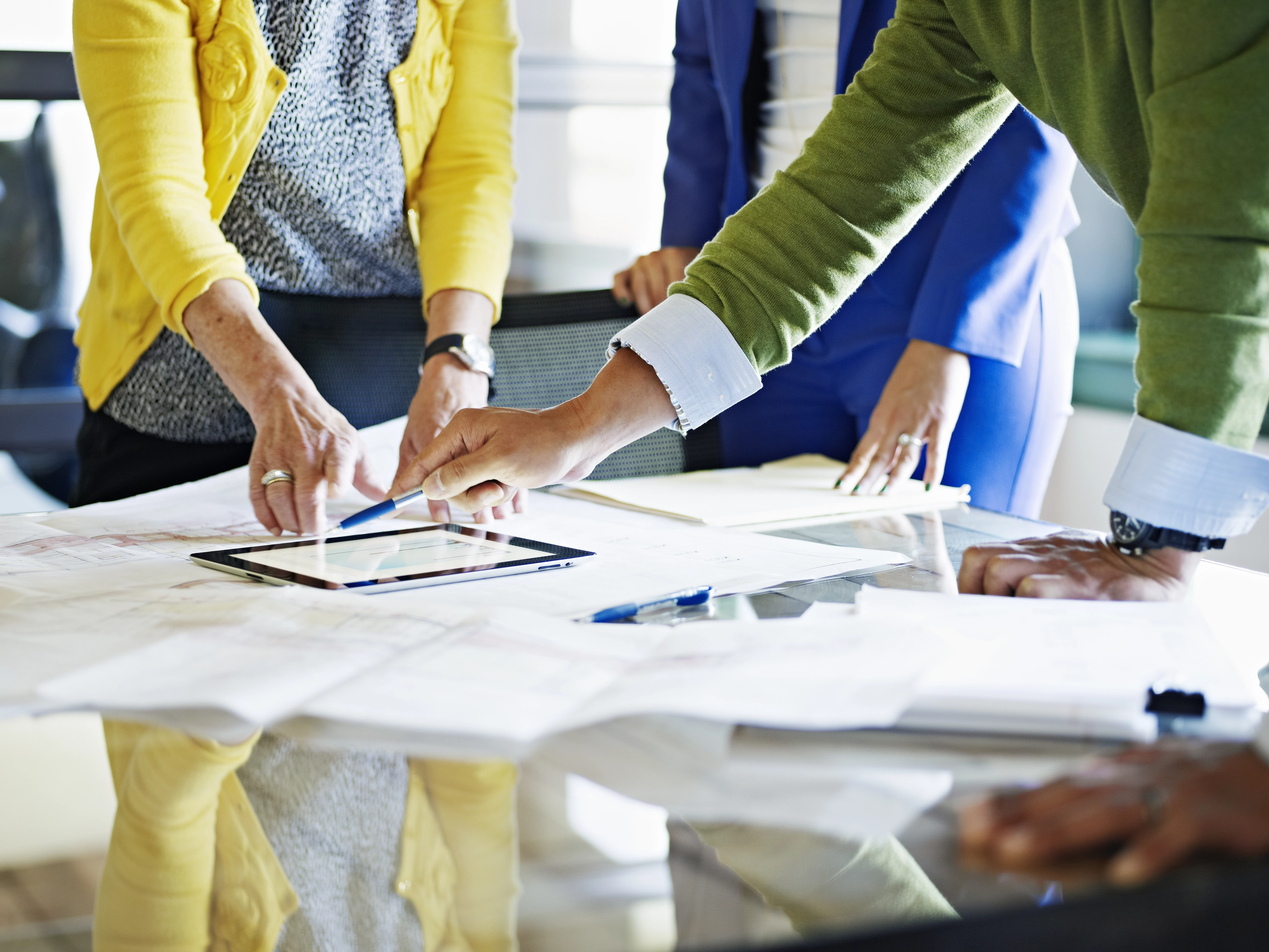 Coworkers discussing project in office conference room looking at plans and digital tablet on table