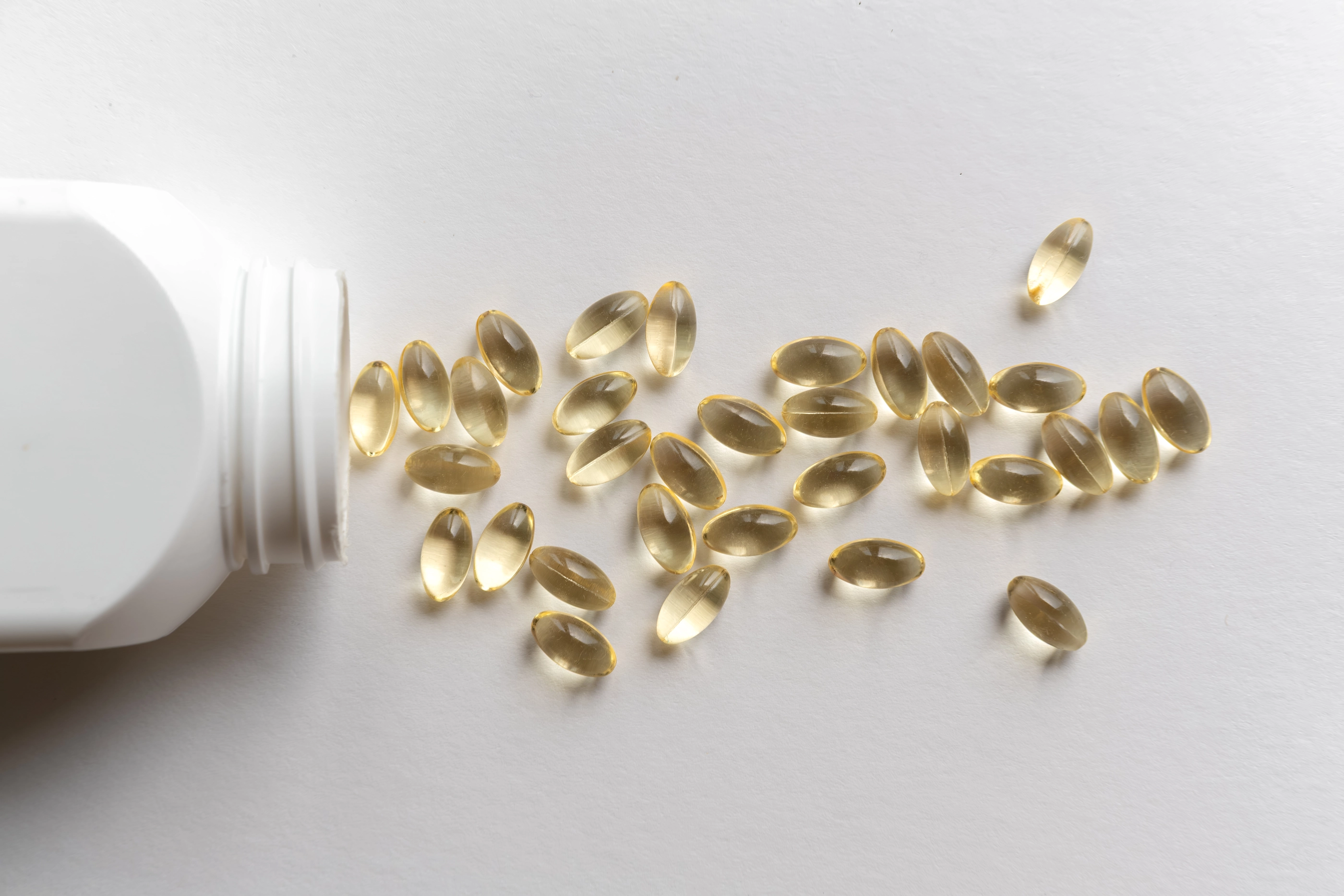 Scattered capsules surround an open white bottle ,  dietary supplements and their role in health and wellness , pharmaceutical products and health-related concepts in a minimalist setting