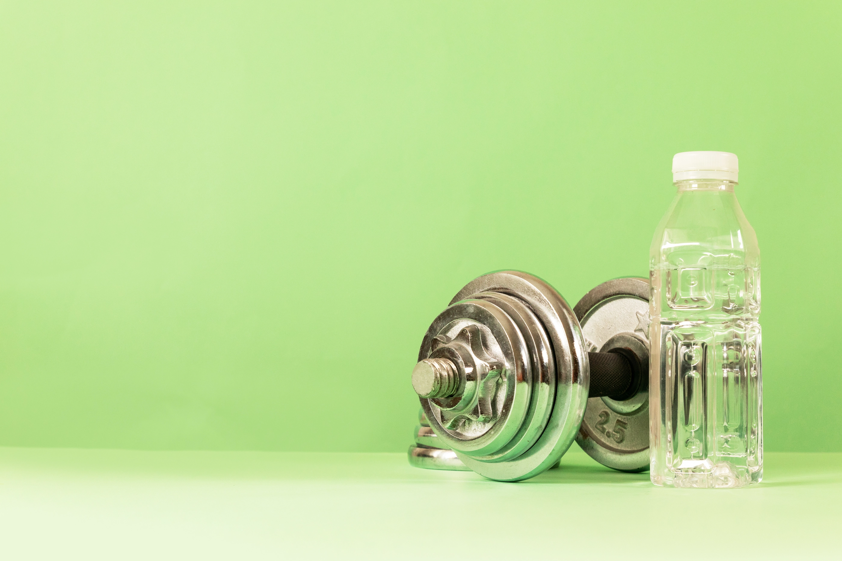 Professional dumbbell for fitness and bodybuilding with a bottle of water on a green background.
