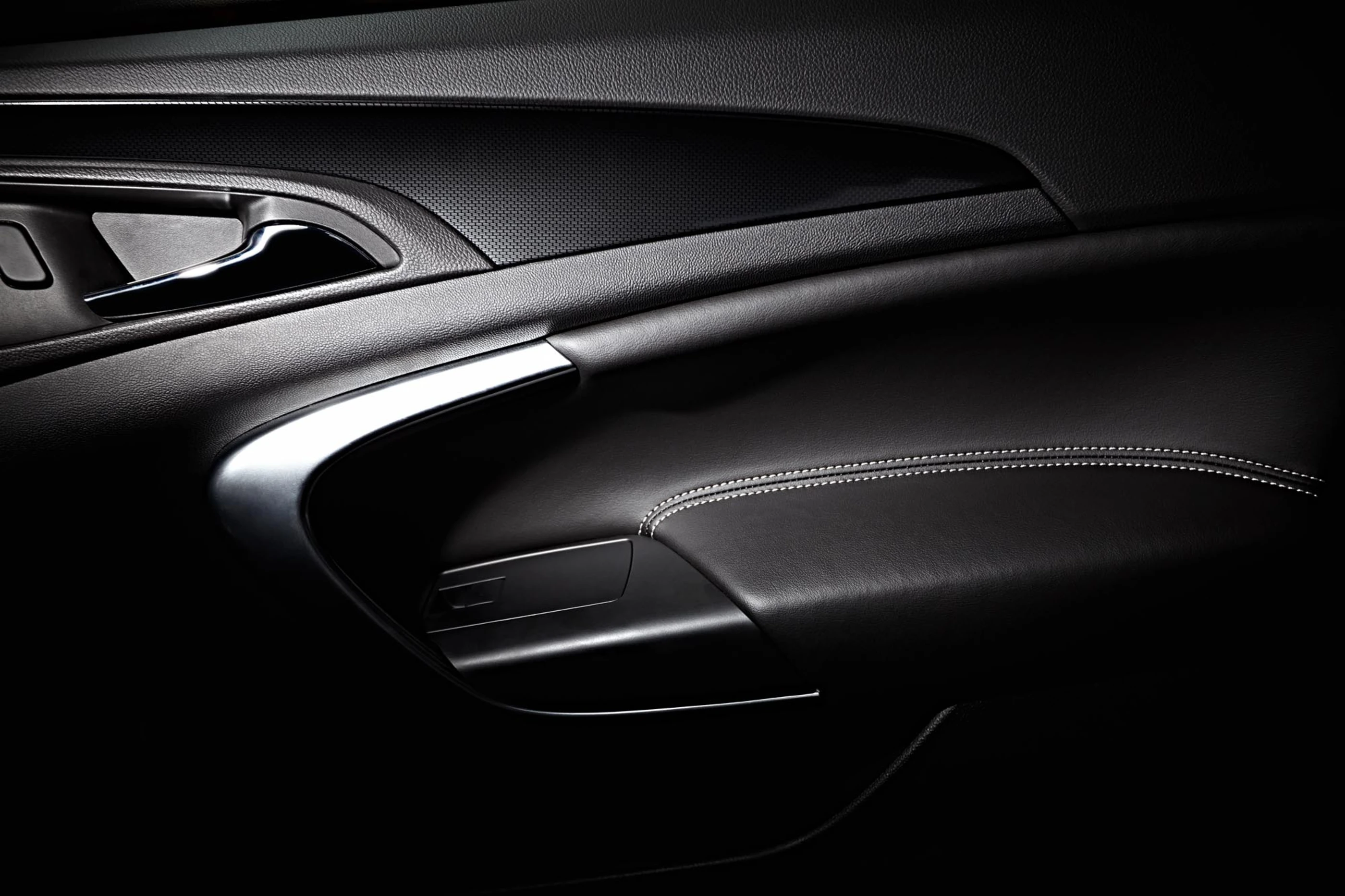 Black leather and plastic on the inside of a car door showing grain and patterns.