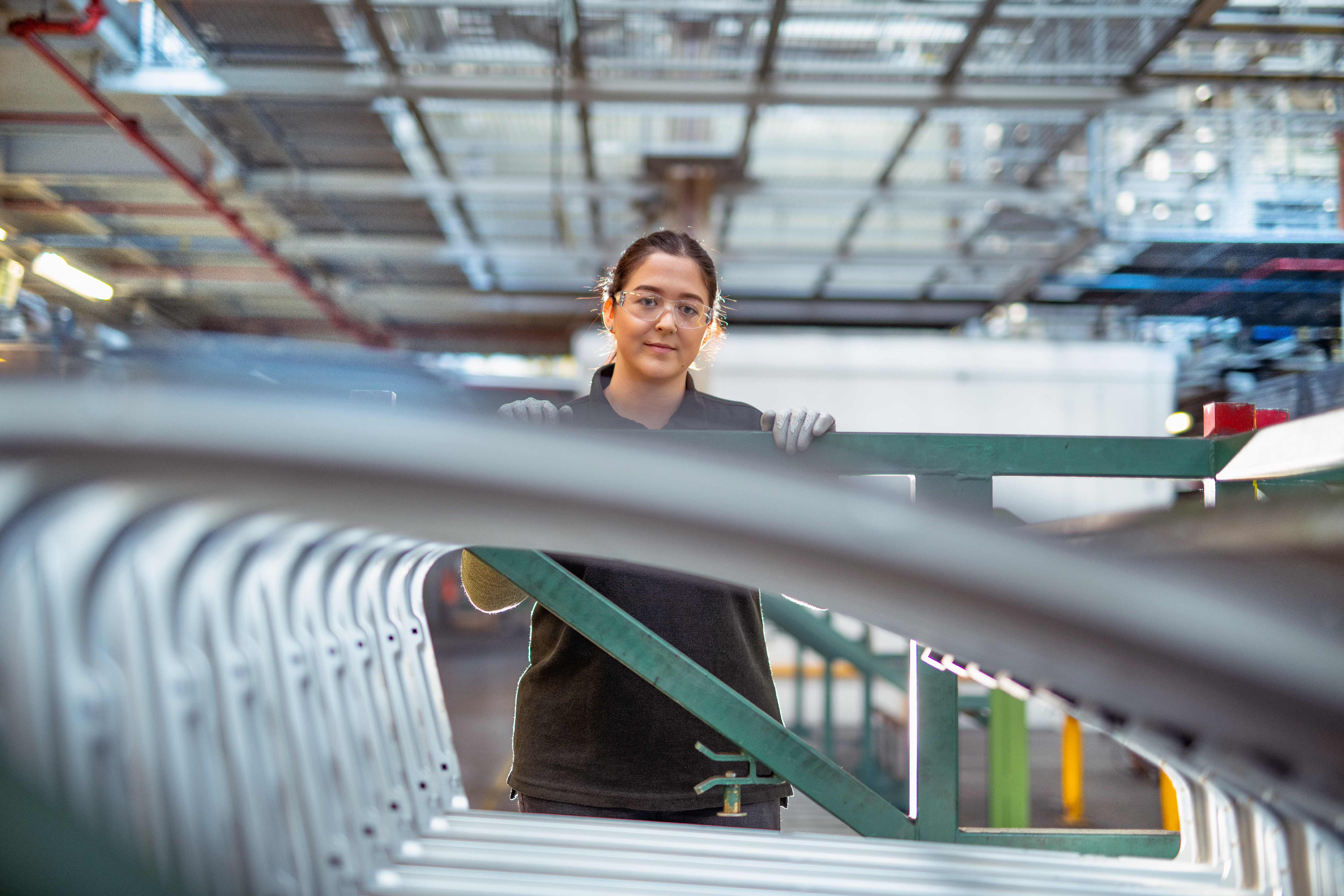 50-50 Portrait of female apprentice with car parts in car factory.