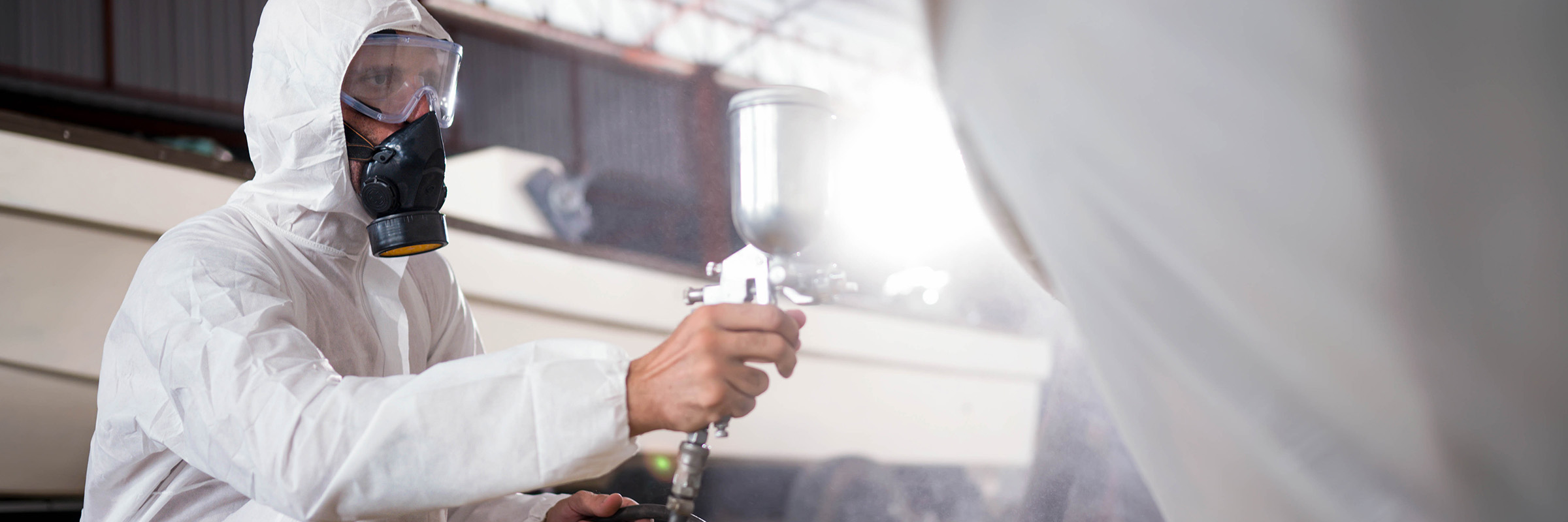 Focus Areas Man applying color on a boat hull outer surface by paint spray gun.